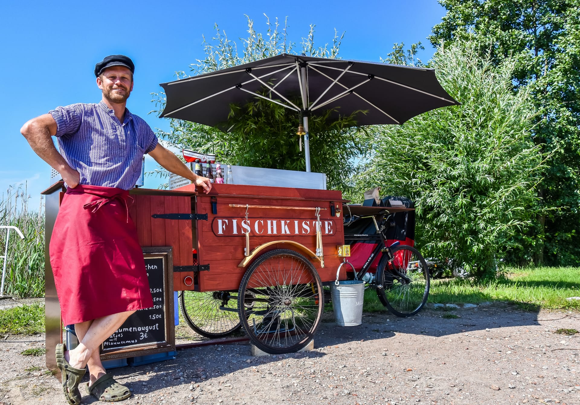 Mann steht an mobiler Fischkiste auf Fahrradanhänger im Grünen